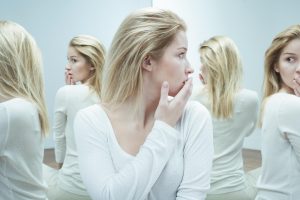 blond woman in a white top with her back to a mirror and two different image in the mirror, surprising and confusing her