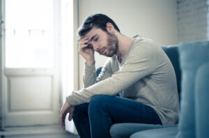 Unhappy and upset Caucasian male on a sofa by himself, alone in the room, looking down, one hand to forehead