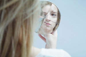 Young blond woman staring into a broken hand mirror with a blank look on her face