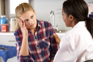 A serious and concerned young woman in a check flannel shirt talking with a female doctor