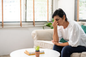Stressed middle-aged woman sitting alone on a couch at home, head in her hand in thought and worry