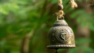 brass Tibetan bell hanging on a rope with out-of-focus trees in the backgroung - Image by Jeanette Atherton