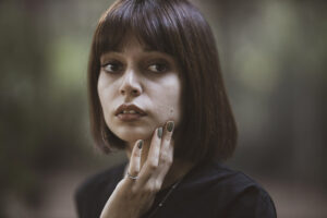 closeup color photo of young brunette woman with gray painted fingernails and a serious or worried expression on her face