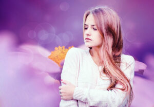 young woman with long strawberry blond hair and a serious worried look on her face in front of an out-of-focus purple and lavender background
