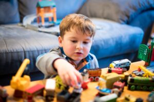 young boy about 4 years old playing with many toys on a coffee table in front of a blue couch