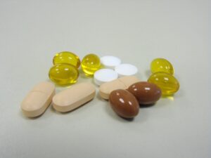 Tan oblong medication tablets, round white pills, brown softgels, and translucent yellow softgels lie on a gray background.