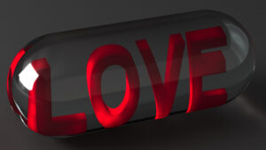The image is of a crystal-clear container in the shape of a medicine capsule with the word "LOVE" in large red three-dimensional letters floating within the capsule shape. The letters are lit by a light source to the left enhancing the three-dimensional characteristics.
